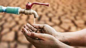 Wassertropfen aus einem Wasserhahn tropfen vor einem vertrockneten Boden in menschliche Hände