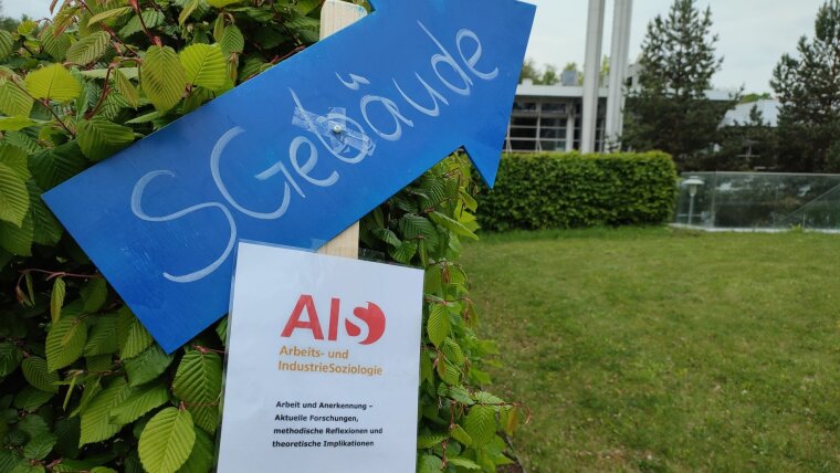 Ein blauer Wegweiser mit der Aufschrift SGebäude und ein Schild mit der Aufschrift Arbeits- und IndustrieSoziologie
