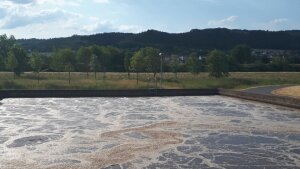 Ein mit Abwasser gefülltes Klärbecken vor der Landschaft des Saaletals