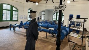 Historischer Raum eines Pumpwerks mit blauen Wasserleitungen im Hintergrund und einem Schild "Museum" im Vordergrund